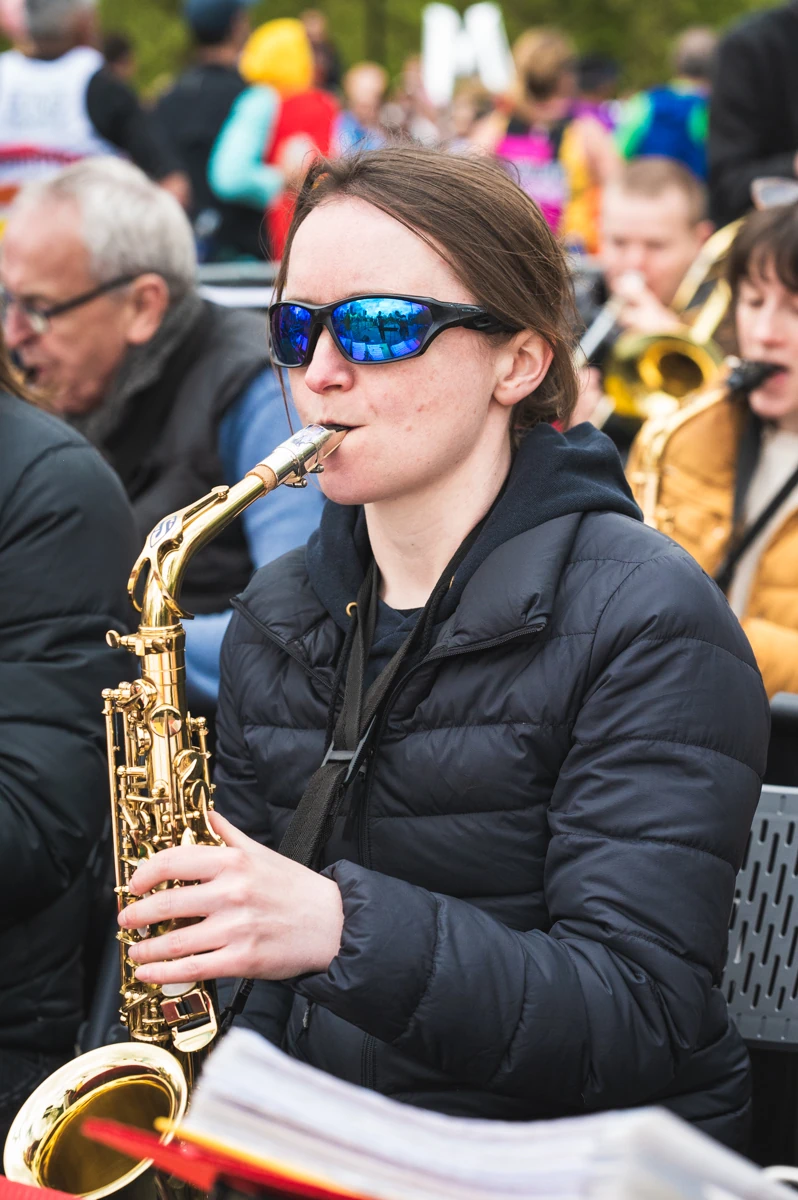 A jazz musician wearing sunglasses and playing an alto saxophone in a band outdoors