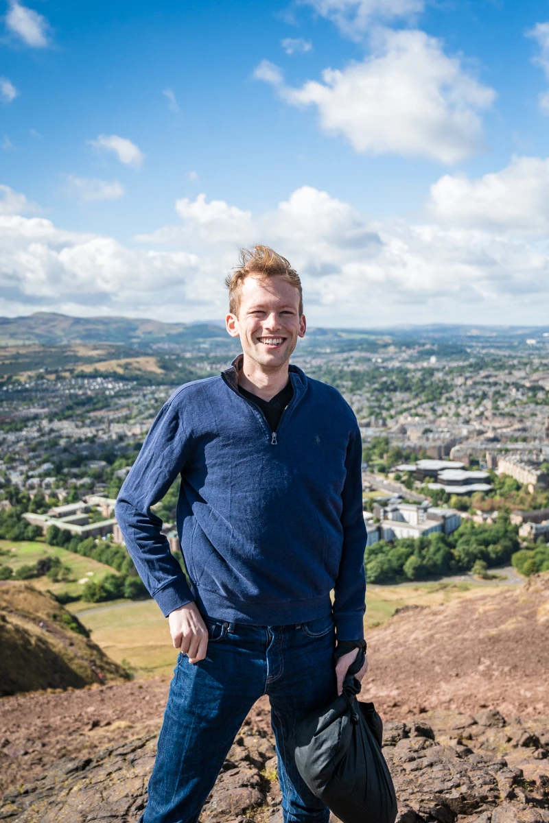 A man at the top of Arthur's Seat in front of the Edinburgh skyline