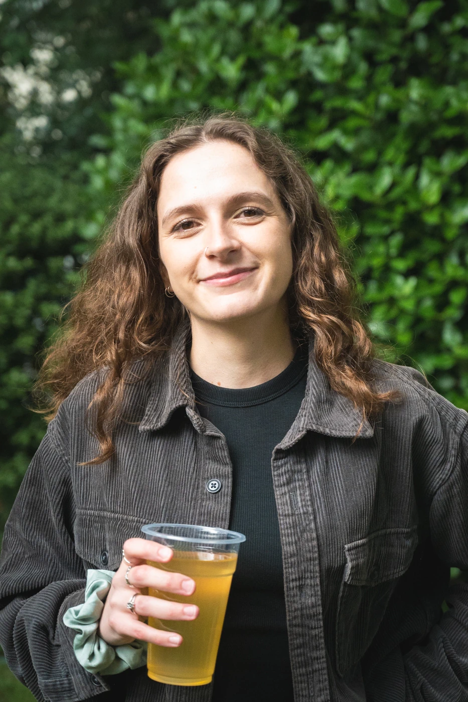 Woman with wavy brown hair holding a drink and smiling