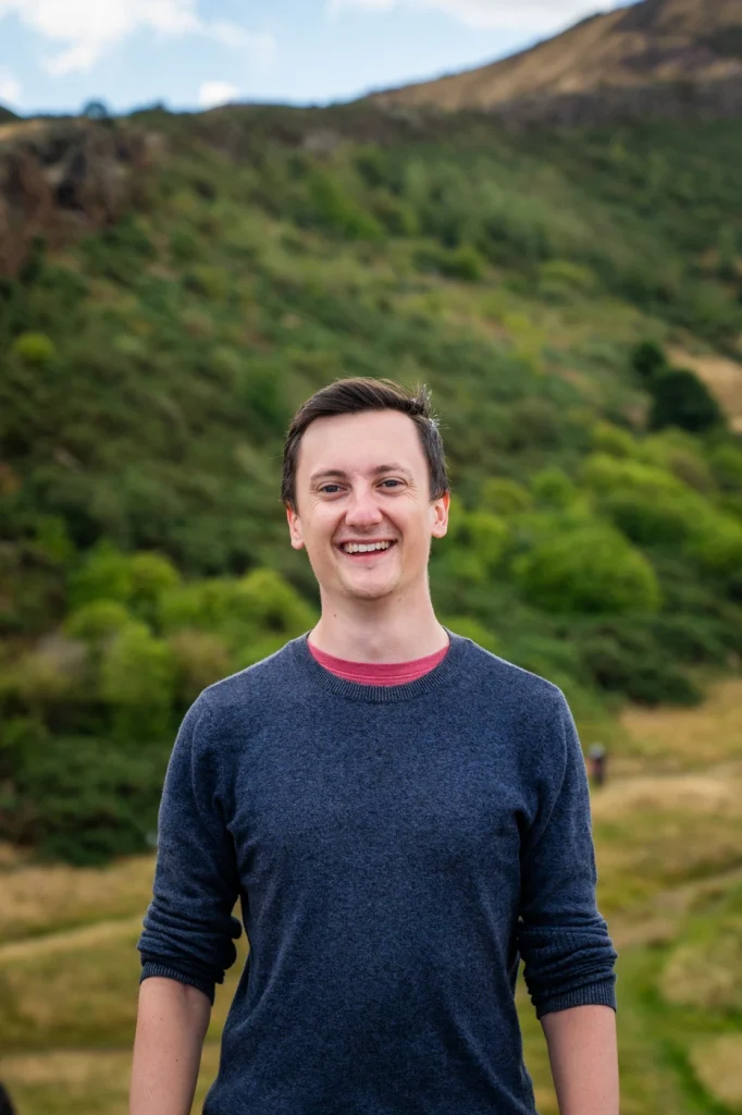 A man outdoors in front of a hill, smiling broadly.