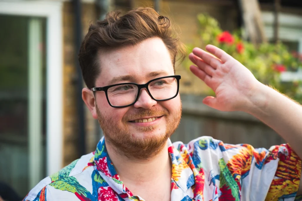 A man with glasses and a colourful shirt, smiling and looking into the distance.
