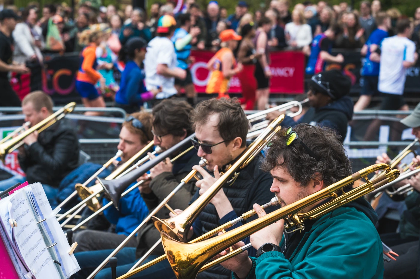 A row of trombones playing jazz in front of a colourful backdrop of runners.