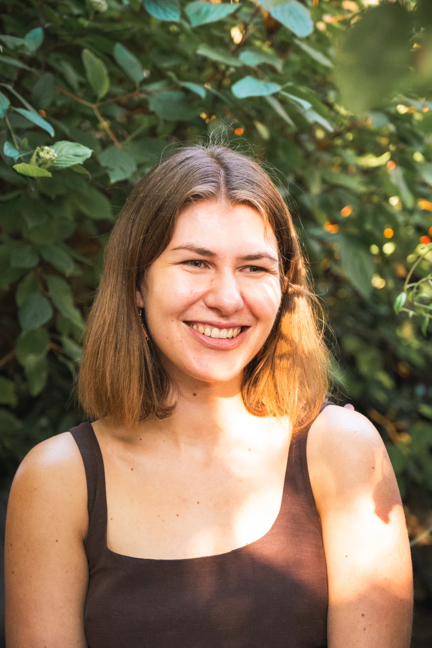 A women standing outdoors in front of a tree, smiling in the sunshine.