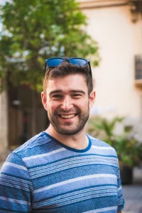 Man in a blue shirt with sunglasses on the top of his head smiling