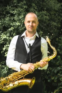 Man in waistcoat holding a tenor saxophone in a garden