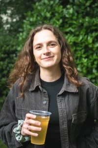 Woman with wavy brown hair holding a drink and smiling