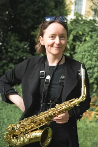 Woman standing in a garden holding an alto saxophone